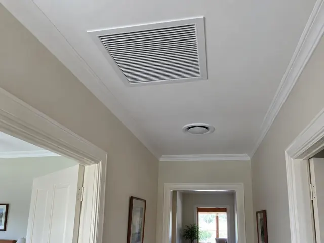 Ceiling return-air grille and round outlet in a painted hallway with timber door trim in Belair