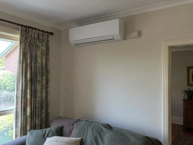 Wall-mounted split system above a lounge sofa in a carpeted living room with curtains in Blackwood